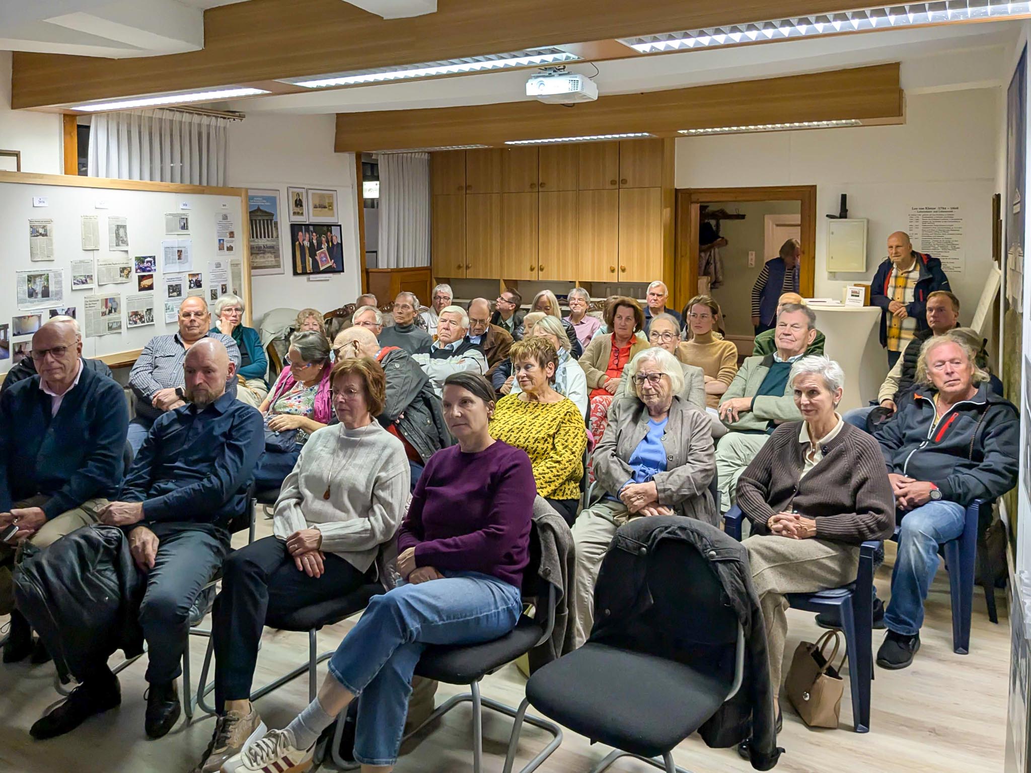 Zahlreiche Zuhörer sitzen bei einem Vortrag im Klenze-Haus in Schladen, an der Wand hängen historische Zeitungsausschüsse und Fotos.