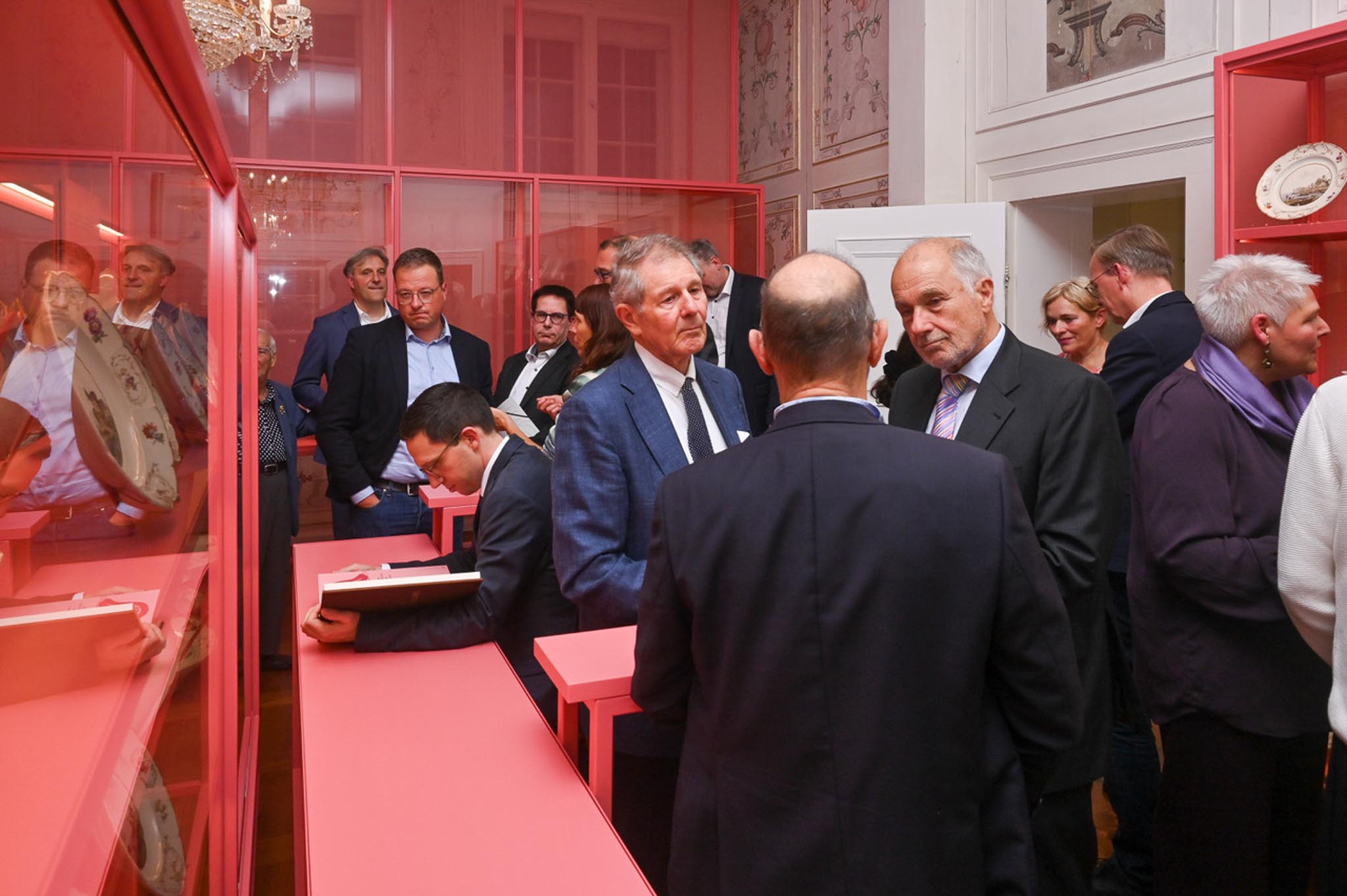 Besucher besichtigen bei der Eröffnung das neue Porzellankabinett mit rosafarbenen Vitrinen und ausgestelltem weißem Porzellan.